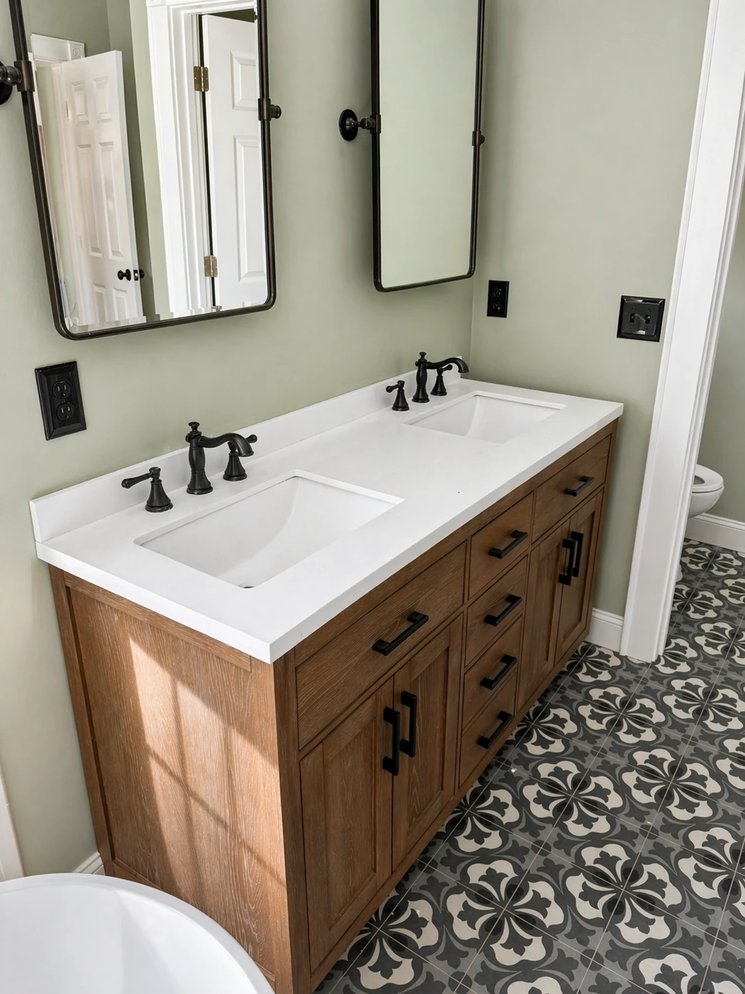 Homestead Place primary bathroom — custom wood double vanity with undermount sinks, arched pivot mirrors, and patterned cement tile floor