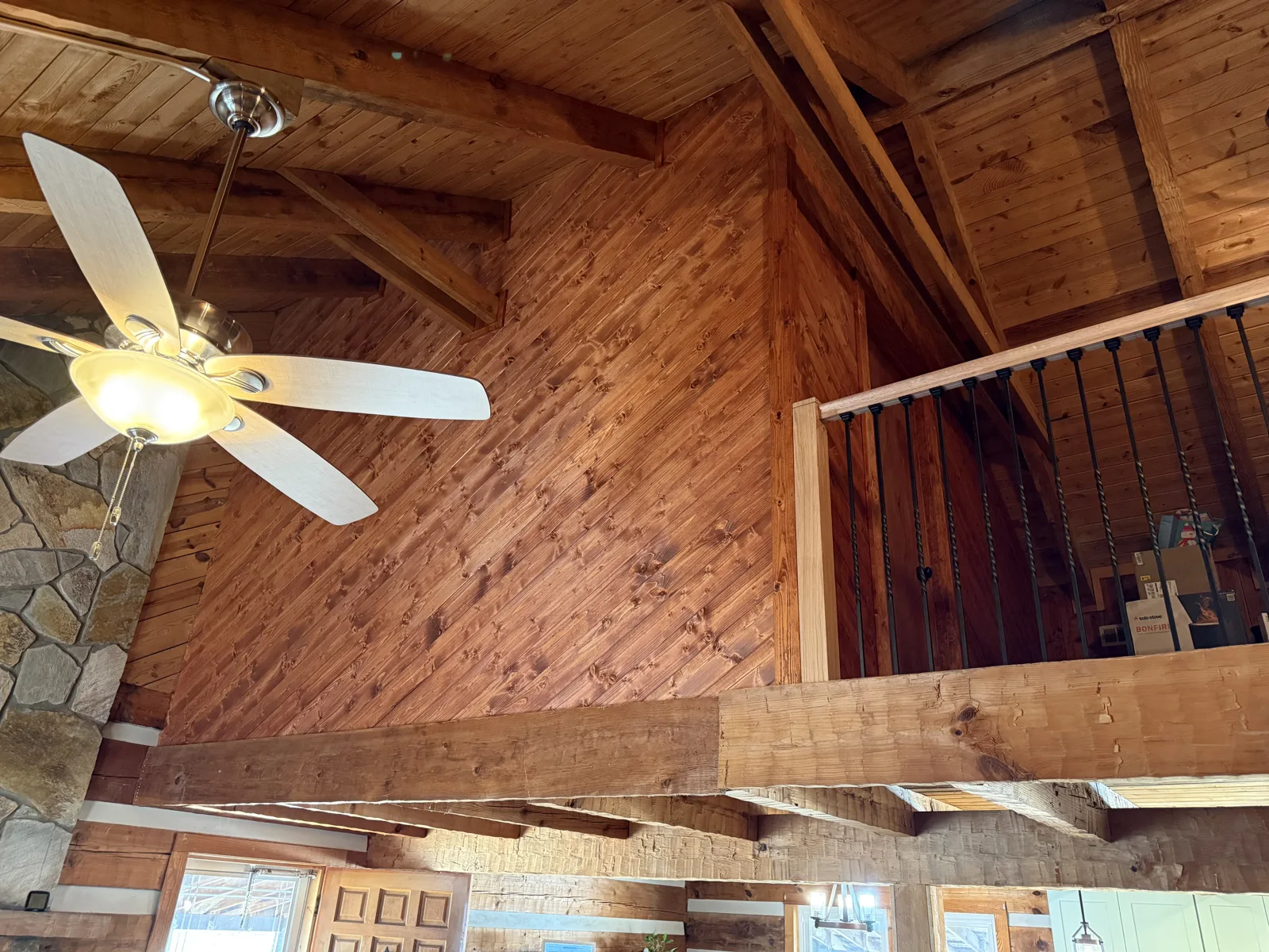 Log cabin great room with stained pine walls, exposed beams and loft railing — Fip Newsome Road renovation in Tobaccoville, NC