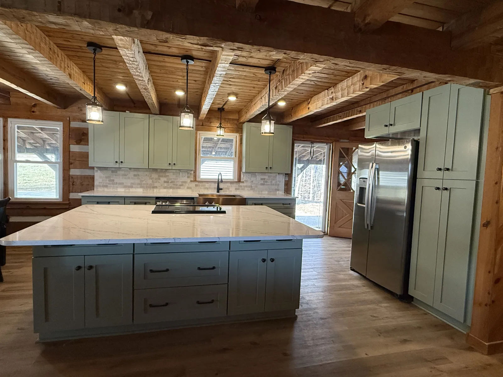 Log cabin kitchen with sage green shaker cabinets, quartz island and stainless appliances under exposed beams — Tobaccoville, NC