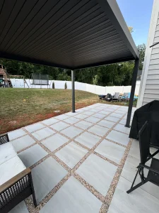 Large-format concrete paver patio with pebble joints beneath a black louvered pergola — backyard hardscape by Salem Builders